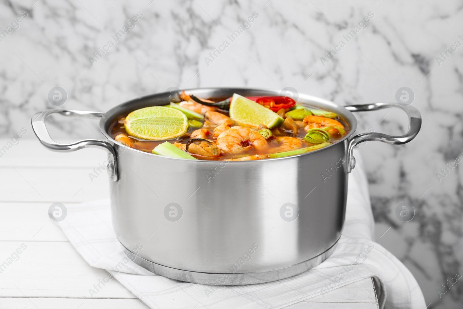 Photo of Saucepan with delicious Tom Yum soup on white wooden table