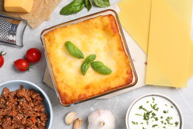 Photo of Tasty cooked lasagna in baking dish and ingredients on light table, flat lay