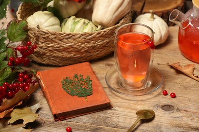 Photo of Delicious viburnum tea, book and pumpkins on wooden table. Cozy autumn atmosphere