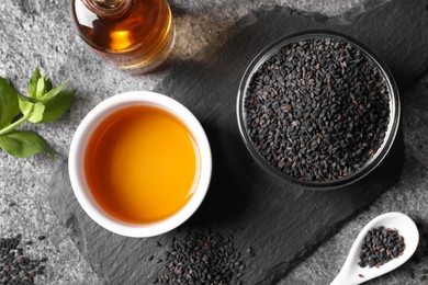 Photo of Black sesame seeds and oil on grey table, flat lay