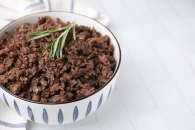 Photo of Fried ground meat in bowl and rosemary on white tiled table, closeup. Space for text