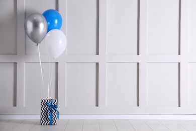 Photo of Gift box and balloons near white wall. Space for text