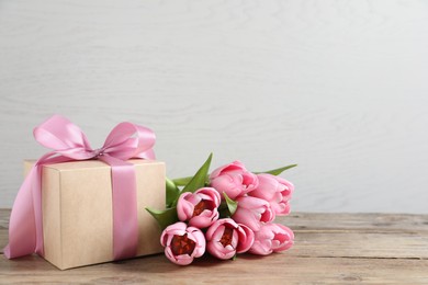 Photo of Gift box and beautiful tulip flowers on wooden table, space for text