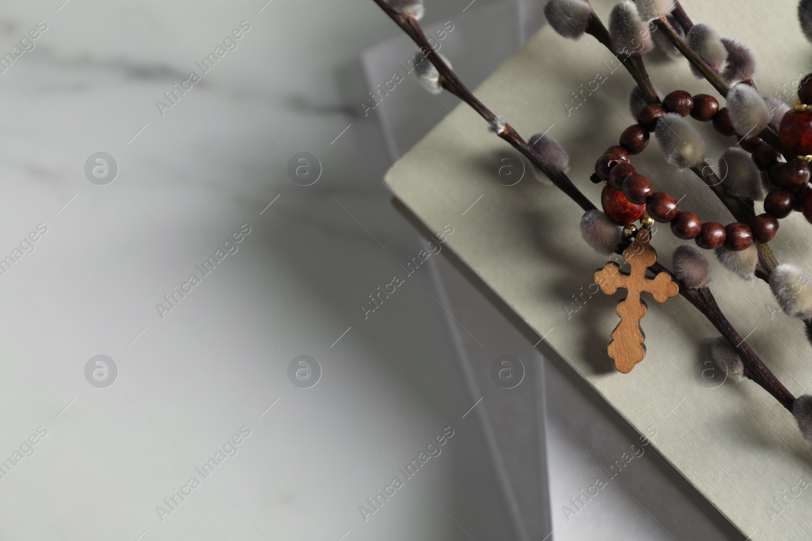 Photo of Rosary beads, books and willow branches on white marble table. Space for text