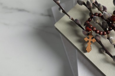 Rosary beads, books and willow branches on white marble table. Space for text