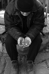 Photo of Poor homeless senior man holding coins outdoors. Black and white effect