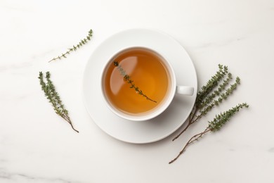 Cup of aromatic herbal tea with thyme on white marble table, flat lay