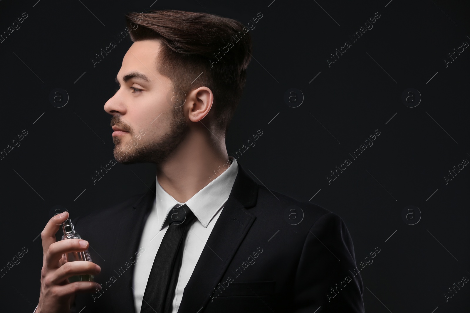 Photo of Handsome man in suit using perfume on dark background