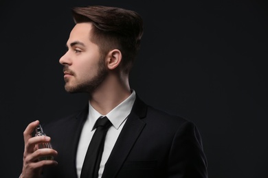 Photo of Handsome man in suit using perfume on dark background