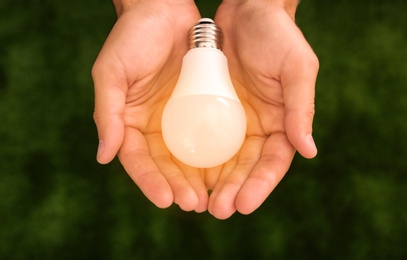 Photo of Man holding lamp bulb against green background, top view