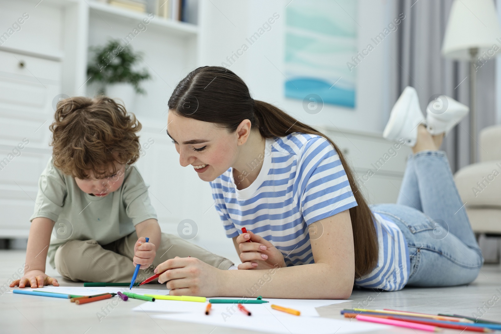 Photo of Mother and her little son drawing with colorful markers on floor at home