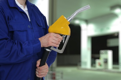 Worker holding fuel nozzle near gas station, closeup