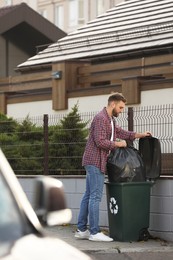 Man putting garbage bag into recycling bin outdoors