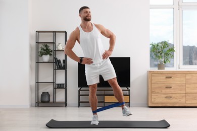 Athletic man doing exercise with elastic resistance band on mat at home