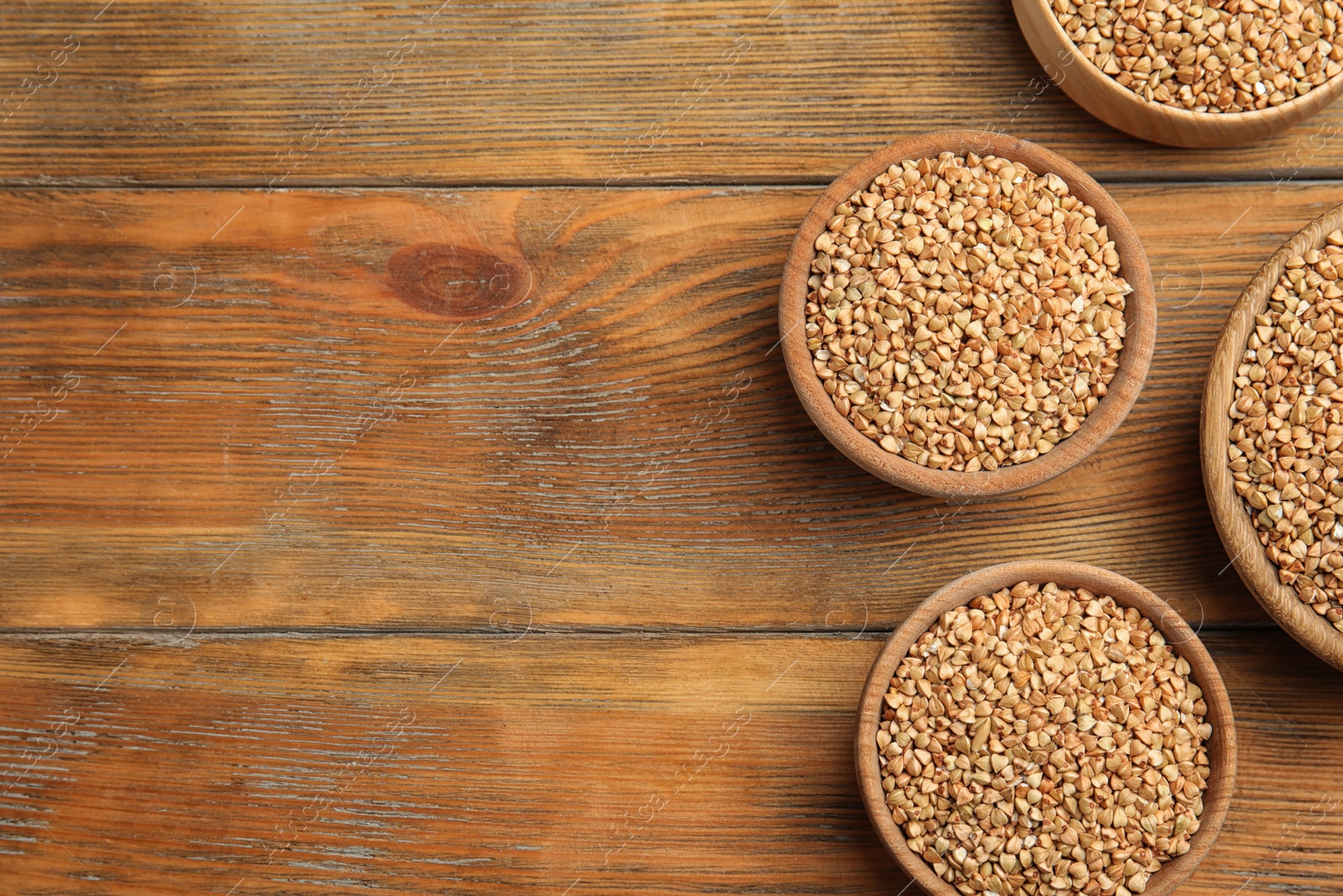 Photo of Uncooked green buckwheat grains in bowls on wooden table, flat lay. Space for text