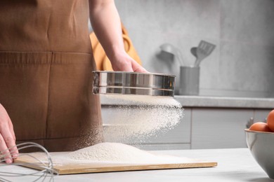 Woman sieving flour at table in kitchen, closeup