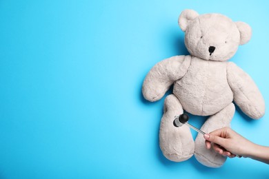 Photo of Woman pretending to test teddy bear's reflexes with hammer on light blue background, closeup and space for text. Nervous system diagnostic