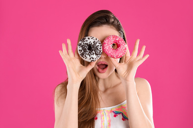 Beautiful young woman with donuts on pink background