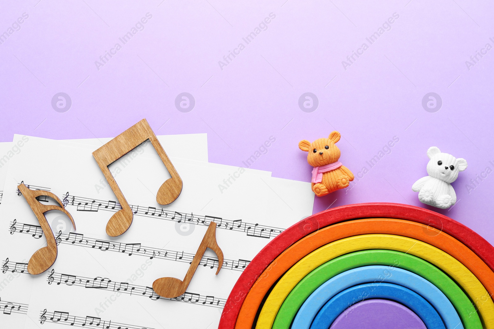 Photo of Wooden notes, music sheets and toys on violet background, top view with space for text. Baby song concept