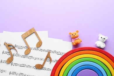Photo of Wooden notes, music sheets and toys on violet background, top view with space for text. Baby song concept