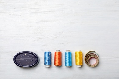 Photo of Color sewing threads, needlecase and measuring tape on wooden background, top view