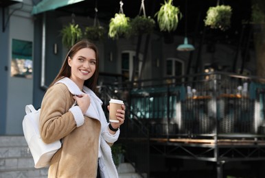 Photo of Young woman with stylish white backpack and cup of drink on city street, space for text