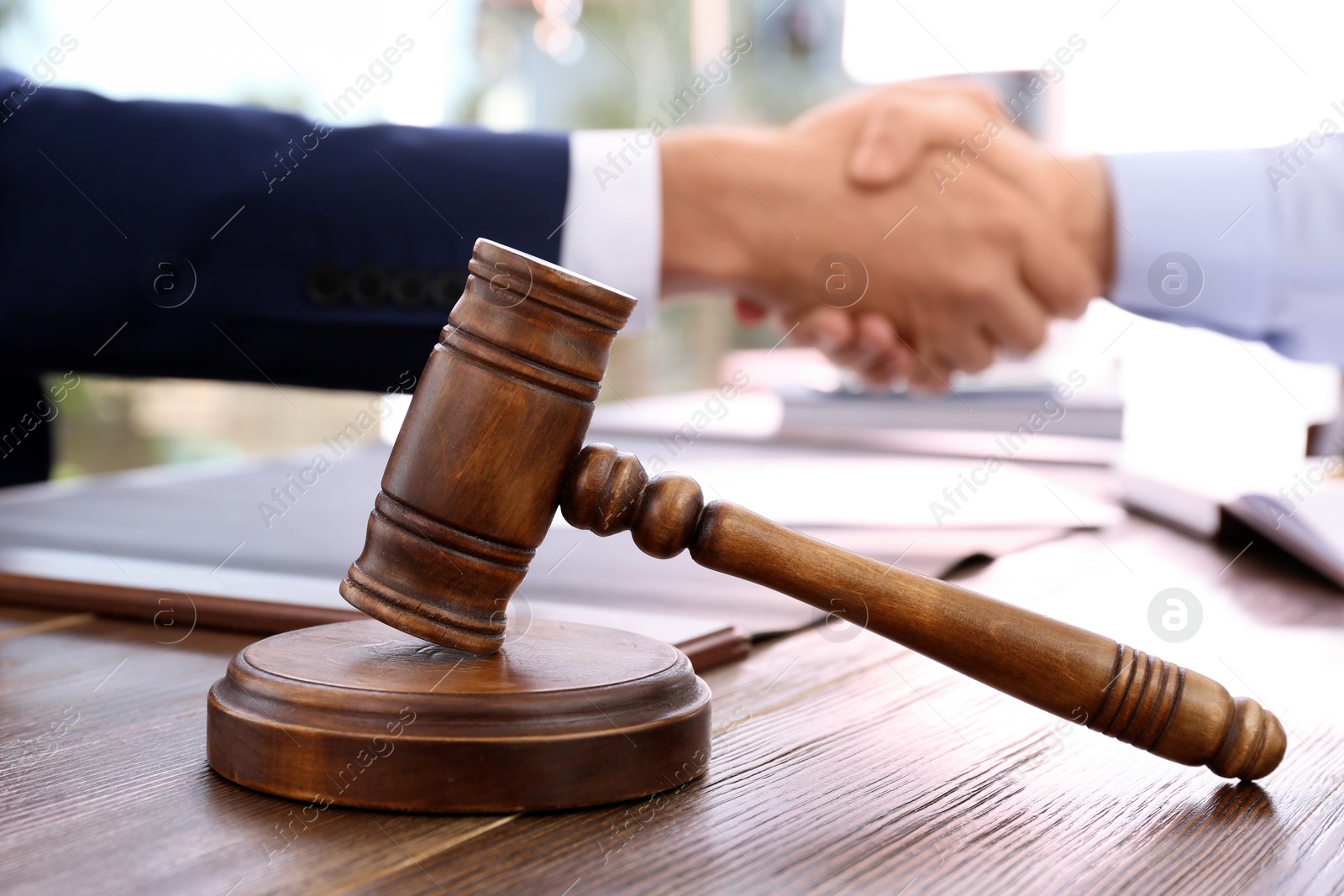 Photo of Gavel and blurred lawyer handshaking with client on background