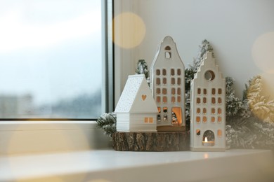 Photo of Beautiful house shaped candle holders and Christmas decor on windowsill indoors, space for text. Bokeh effect