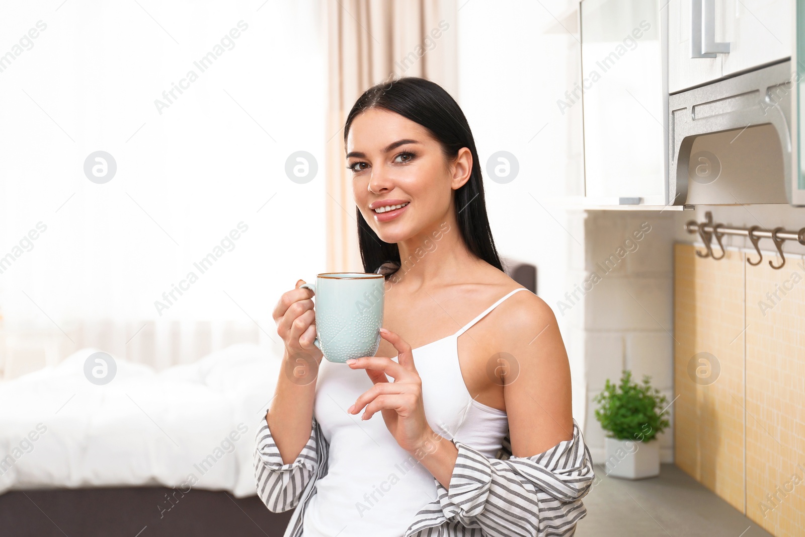 Photo of Beautiful young woman in white underwear drinking coffee at home