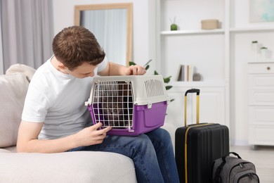 Photo of Travel with pet. Man holding carrier with cute cat on sofa at home