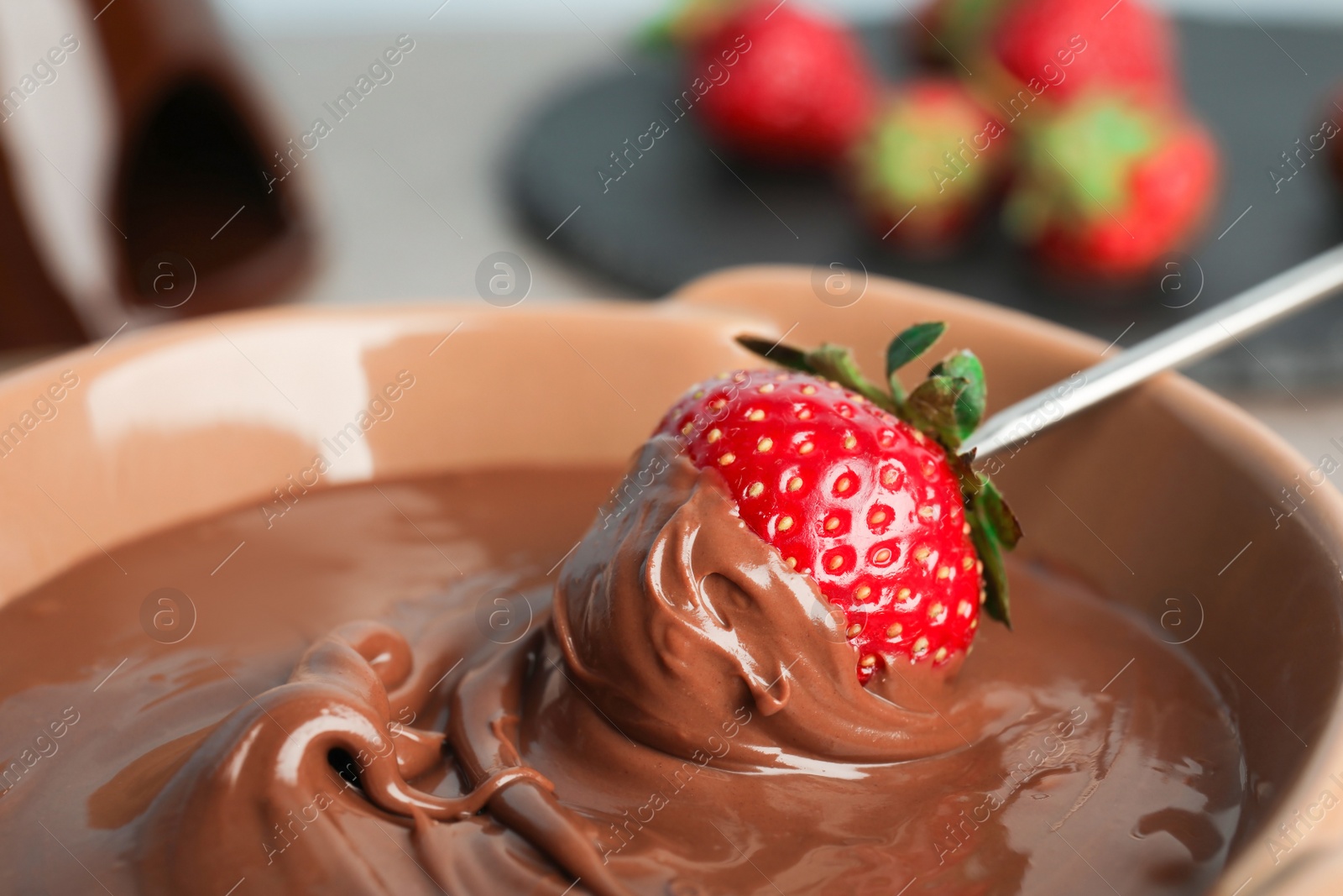 Photo of Ripe strawberry dipping into chocolate fondue, closeup