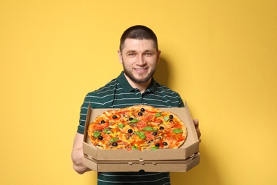 Attractive young man with delicious pizza on color background