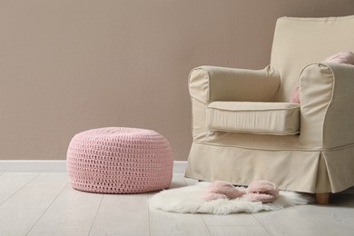 Photo of Knitted pouf, fuzzy rug with slippers and armchair near beige wall indoors. Space for text