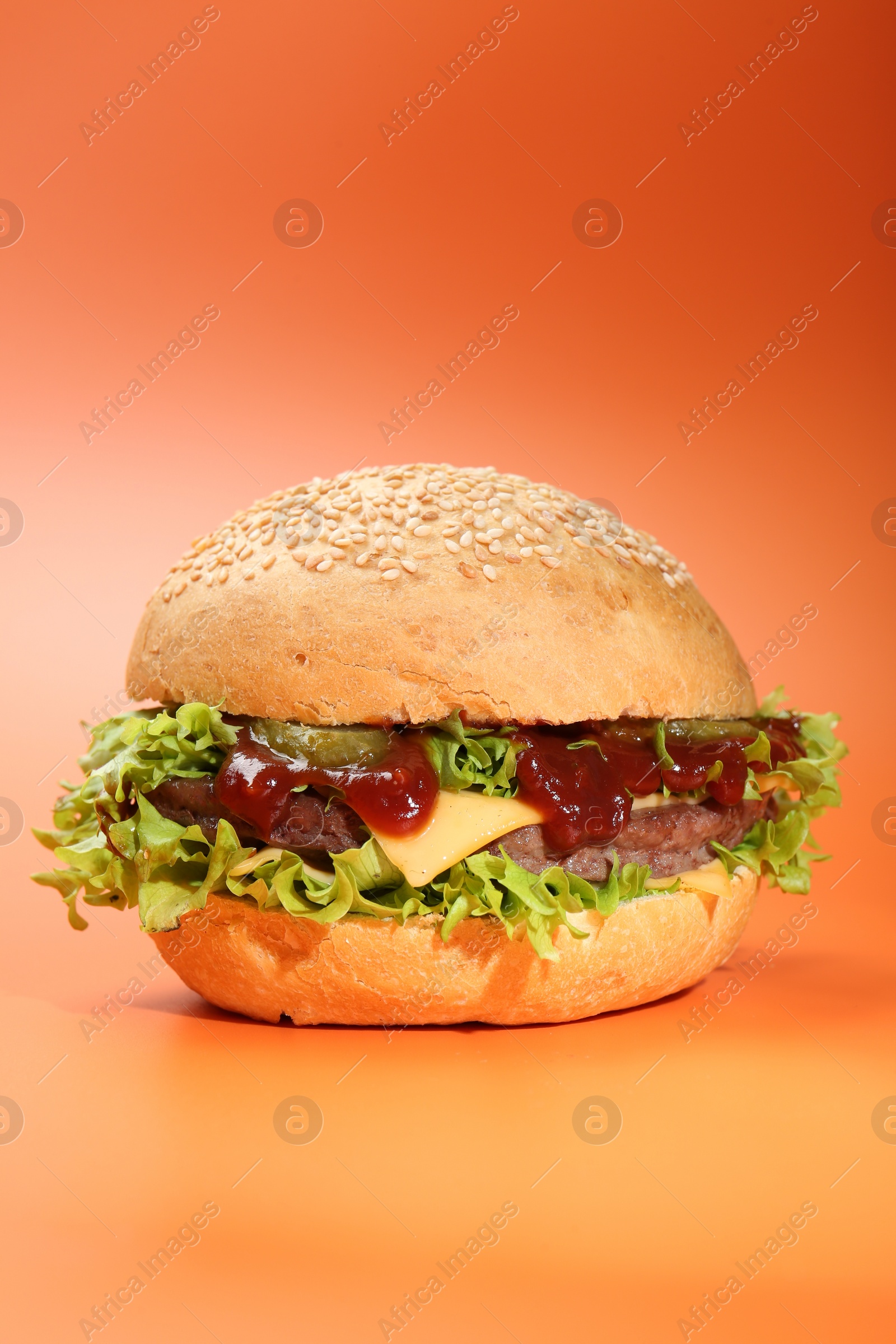 Photo of Delicious cheeseburger with lettuce, pickle, ketchup and patty on coral background