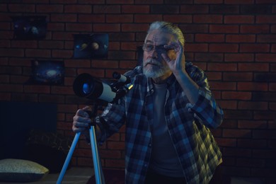 Photo of Senior man using telescope to look at stars in room