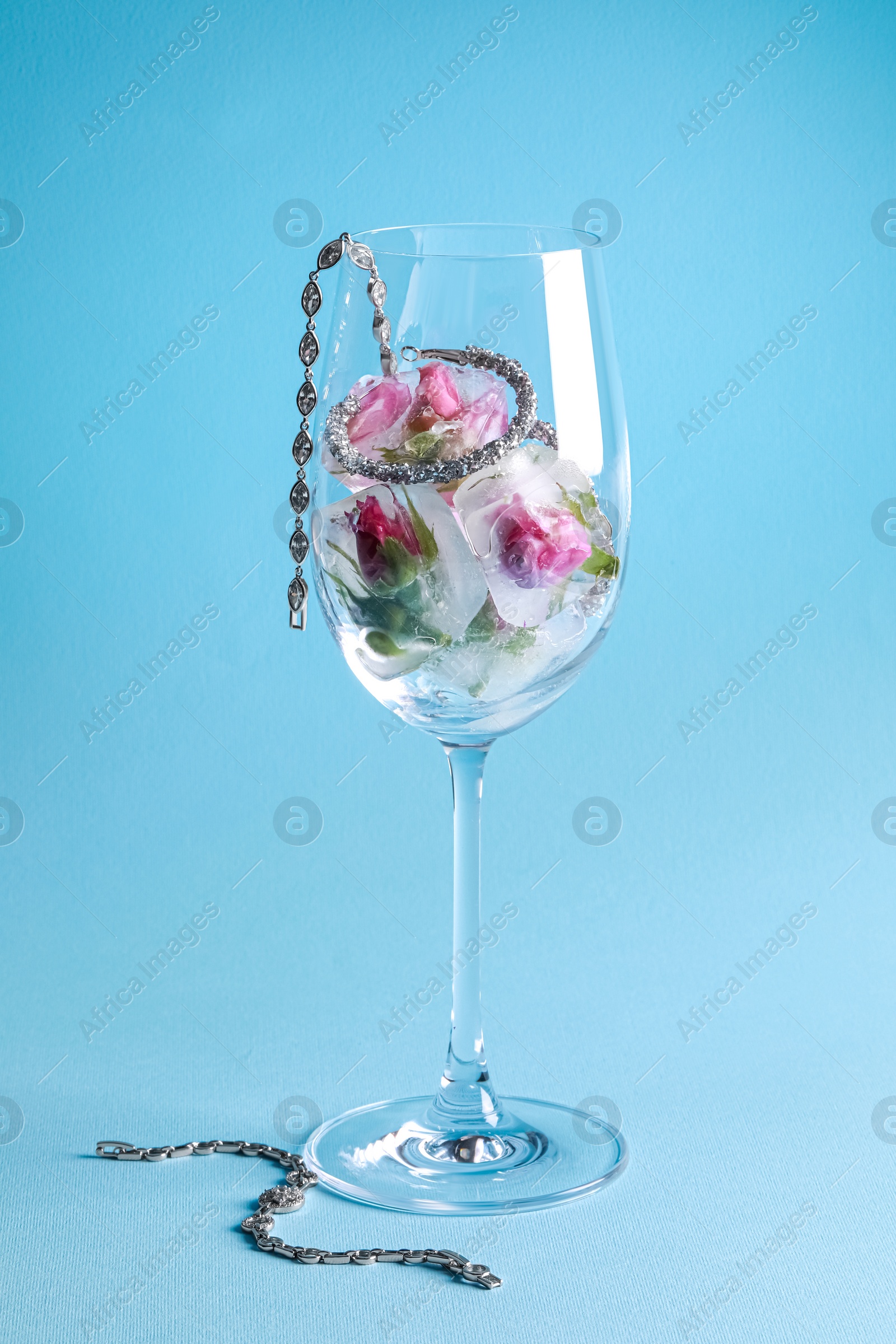 Photo of Elegant jewelry. Stylish presentation with luxury earrings, bracelets and frozen roses in glass on light blue background