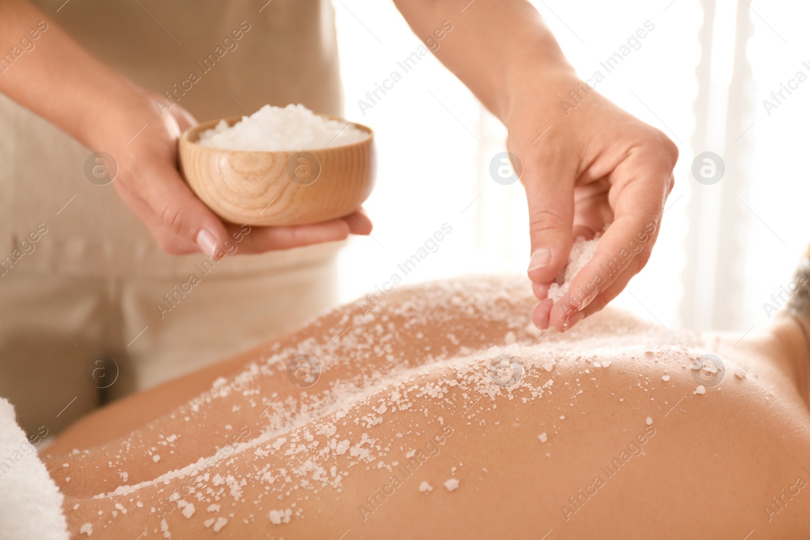 Photo of Young woman having body scrubbing procedure with sea salt in spa salon, closeup