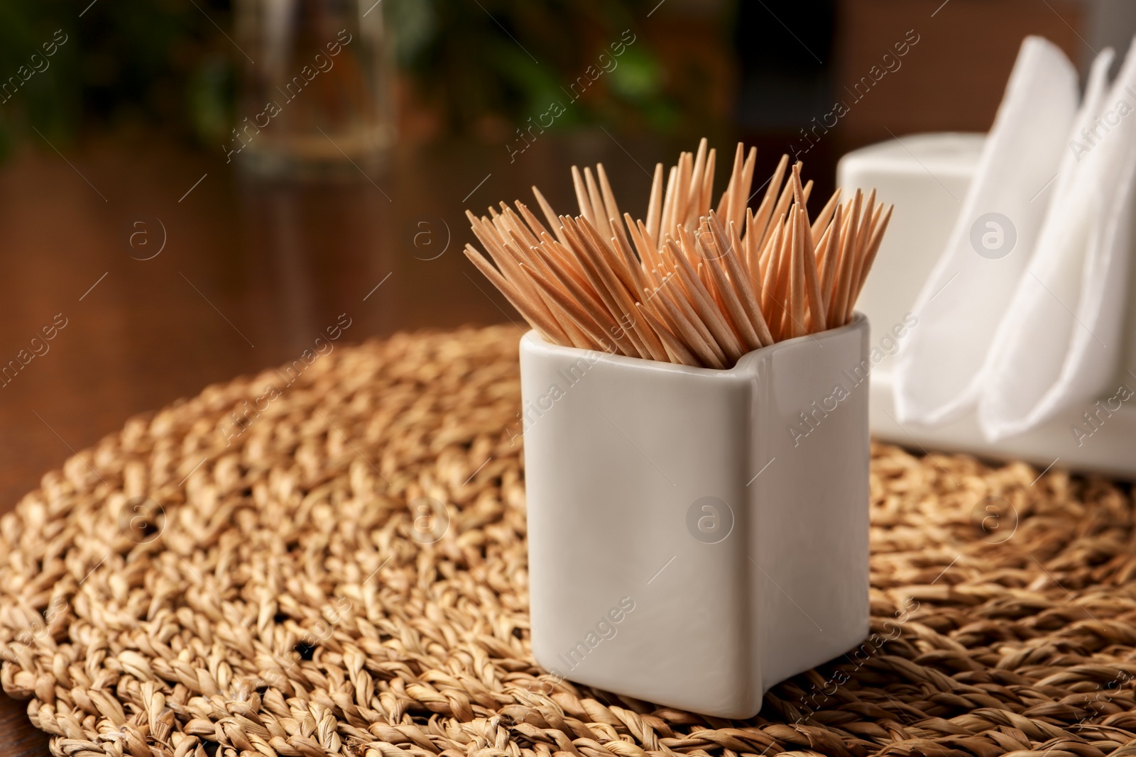 Photo of Wooden holder with many toothpicks on wicker mat, closeup. Space for text