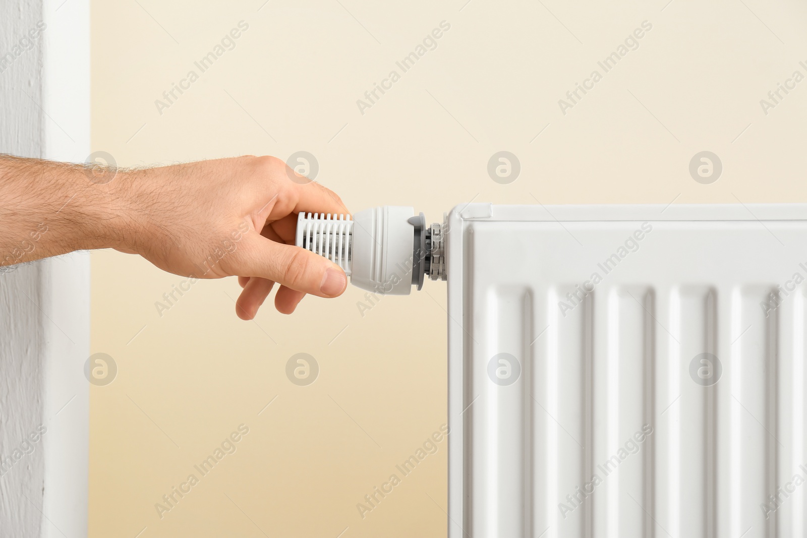 Photo of Man adjusting heating radiator thermostat indoors