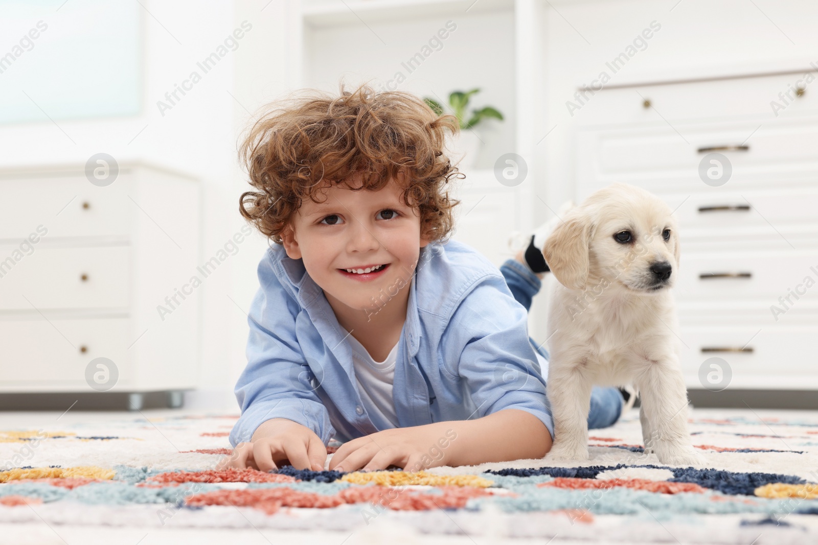 Photo of Little boy lying with cute puppy on carpet at home