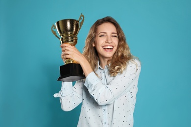 Portrait of happy young woman with gold trophy cup on blue background