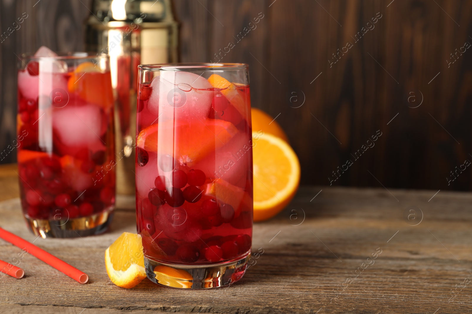 Photo of Tasty cranberry cocktail with ice cubes and orange in glasses on wooden table, space for text