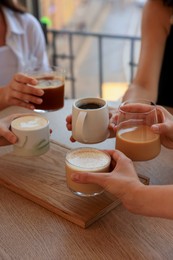 Friends drinking coffee at wooden table in cafe, closeup