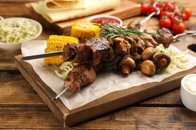 Metal skewers with delicious meat and vegetables served on wooden table