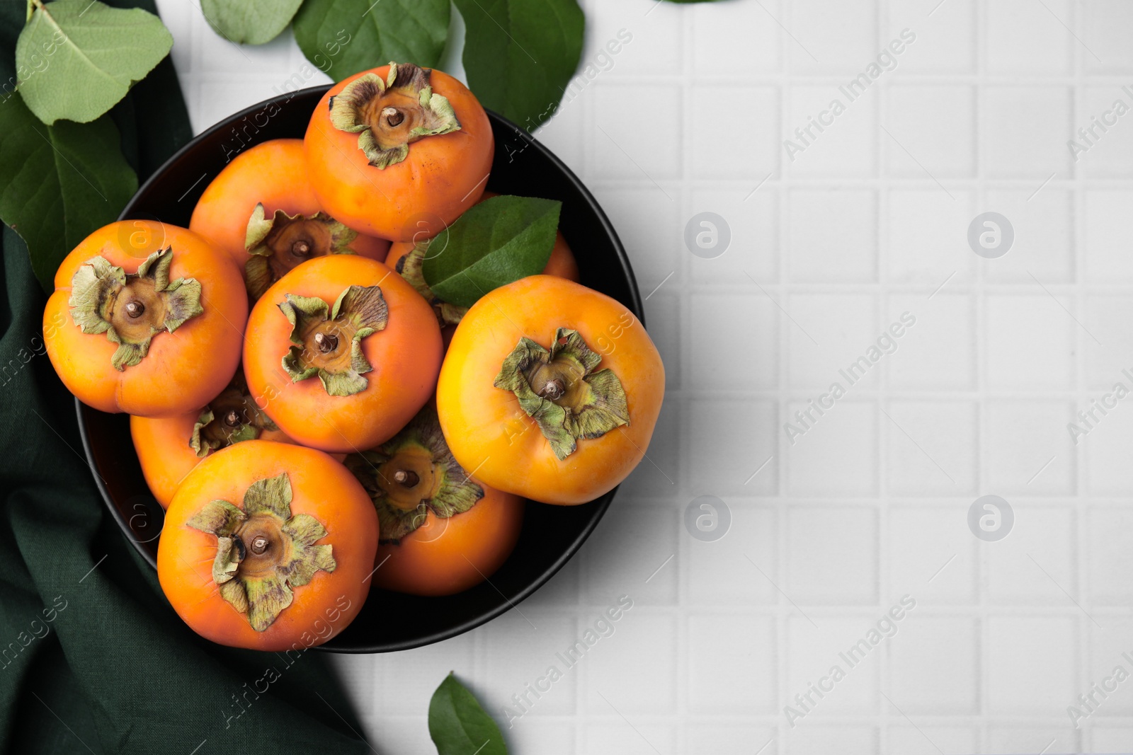 Photo of Bowl with delicious ripe juicy persimmons on white table, flat lay. Space for text