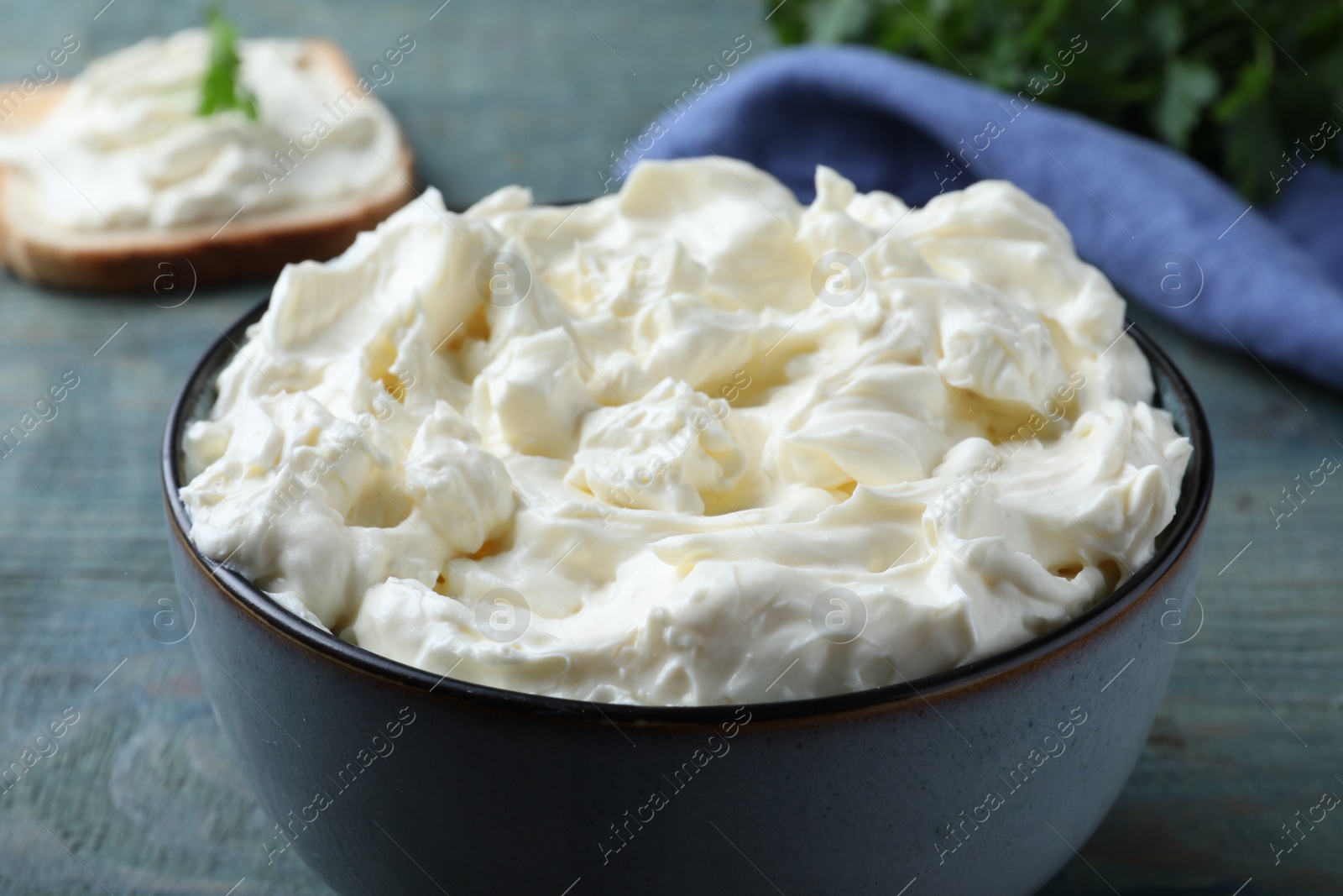 Photo of Tasty cream cheese on light blue wooden table, closeup