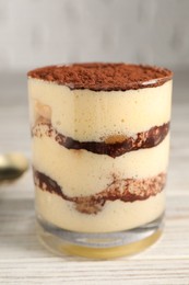 Photo of Delicious tiramisu in glass on light wooden table, closeup