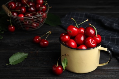 Photo of Metal mug with ripe sweet cherries on dark wooden table. Space for text