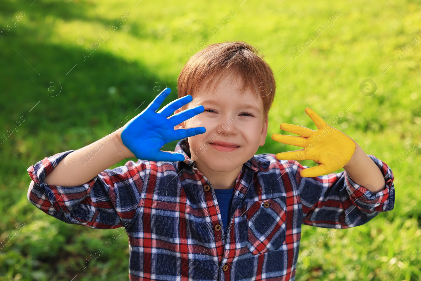 Photo of Little boy with hands painted in Ukrainian flag colors outdoors. Love Ukraine concept