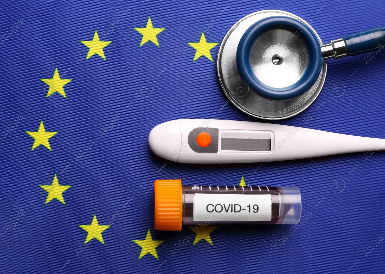 Photo of Test tube with blood sample, thermometer and stethoscope on European Union flag background, flat lay. Coronavirus outbreak
